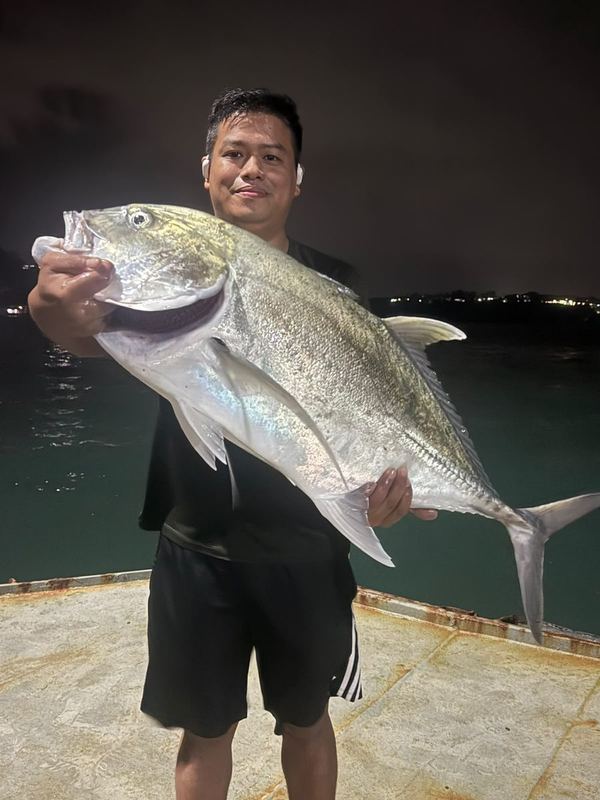 Customer holding a large trevally beside the water at night