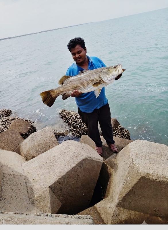 Customer standing on rock armour holding a fish beside the sea
